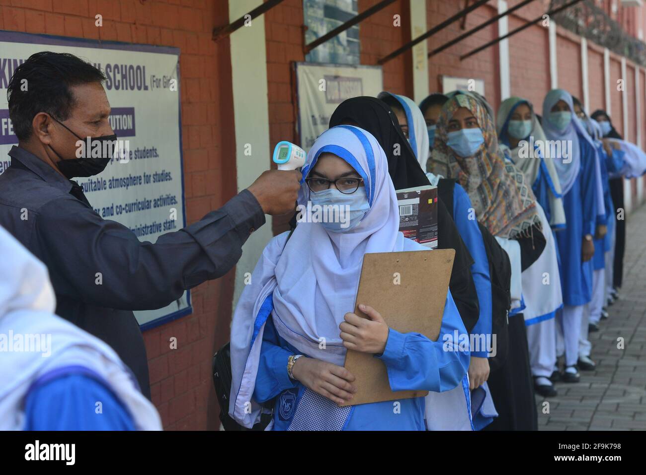 Lahore, Pakistan. 19 Apr 2021. Una guardia di sicurezza sta controllando la temperatura corporea e igienizzando le scarpe delle ragazze studentesse prima di entrare negli Istituti educativi. Governo Kinaird ragazze liceo dal 9 ° al 12 ° grado è riaperto dopo una lunga vacanza a causa della terza fase di Covid-19 a Lahore. (Foto di Rana Sajid Hussain/Pacific Press) Credit: Pacific Press Media Production Corp./Alamy Live News Foto Stock