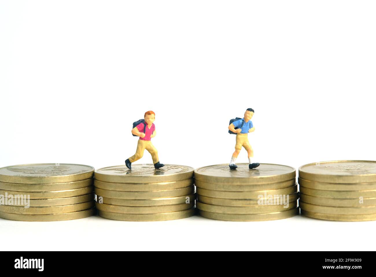 Budget di ingresso alla scuola. Bambini o bambini, camminando sopra la pila di moneta d'oro. Fotographia dei giocattoli della gente piccola in miniatura. Isolato su backgroun bianco Foto Stock
