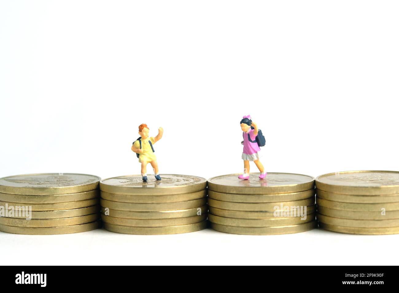 Budget di ingresso alla scuola. Bambini o bambini, camminando sopra la pila di moneta d'oro. Fotographia dei giocattoli della gente piccola in miniatura. Isolato su backgroun bianco Foto Stock