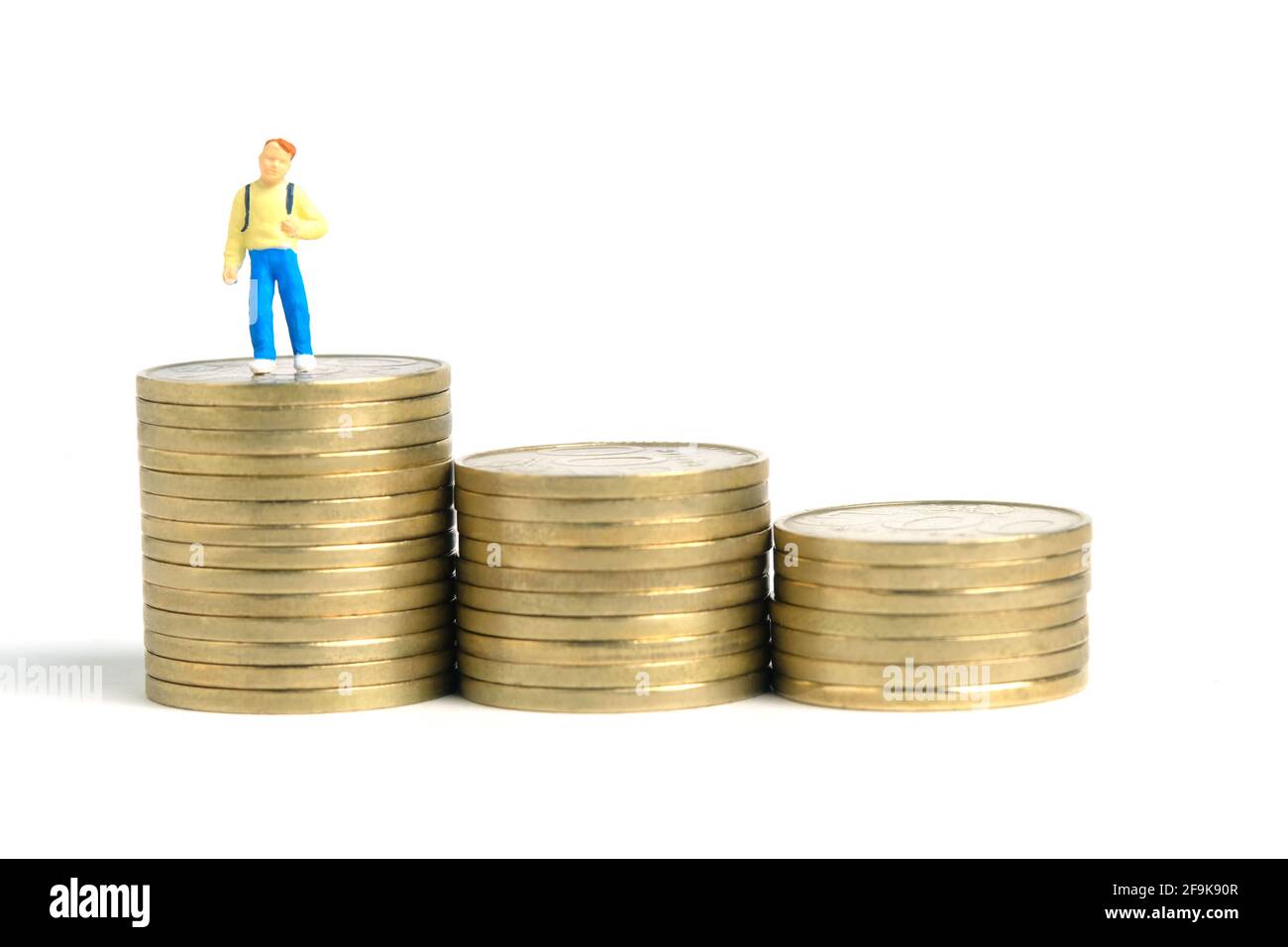 Budget di ingresso alla scuola. Un capretto, in piedi sulla scala superiore della pila di moneta. Fotographia dei giocattoli delle piccole persone in miniatura. Isolato su sfondo bianco. Foto Stock