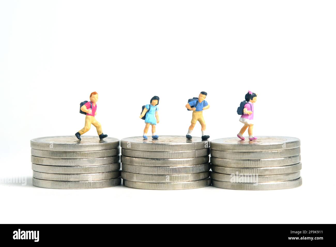 Budget di ingresso alla scuola. Bambini o bambini, camminando sopra la pila di moneta d'oro. Fotographia dei giocattoli della gente piccola in miniatura. Isolato su backgroun bianco Foto Stock