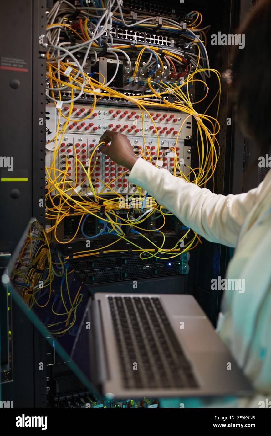 Primo piano verticale di un tecnico di rete femminile che collega i cavi nell'armadietto del server mentre lavora con il supercomputer nel data center, spazio di copia Foto Stock