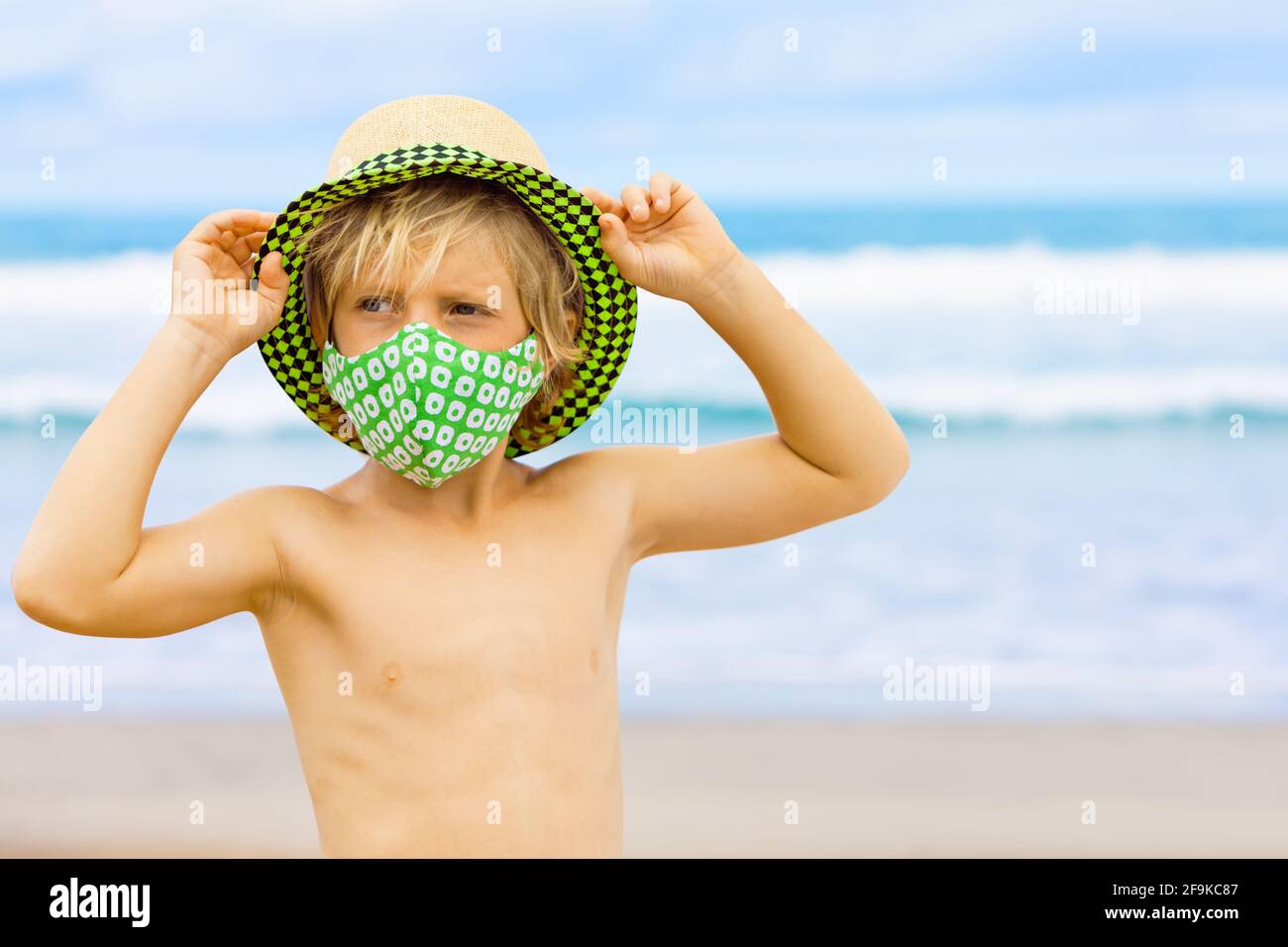 Bambini in cappello di paglia, maschere eleganti divertirsi sulla spiaggia  di mare. Nuove regole per indossare la copertura del viso in luoghi  pubblici. Nuove regole per indossare la maschera di copertura facciale