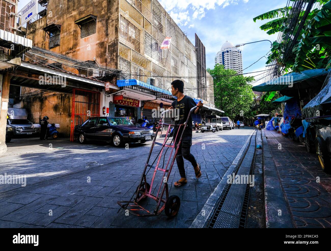 Un giovane spinge un tram vuoto davanti ad alcuni vecchi edifici a Chinatown, Bangkok, Thailandia. Foto Stock