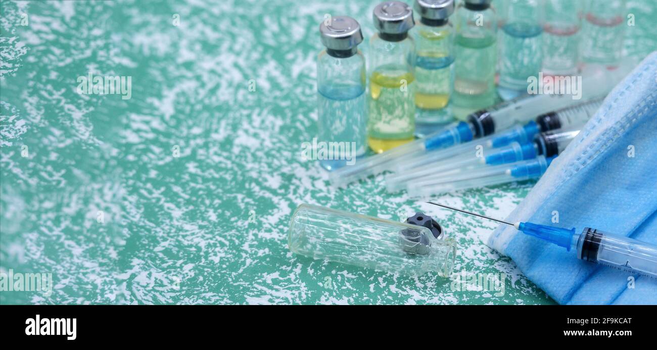 Prevenzione delle malattie stagionali. Fiale mediche, siringhe e una maschera su sfondo verde. Vaccinazione contro covid-19. Foto Stock