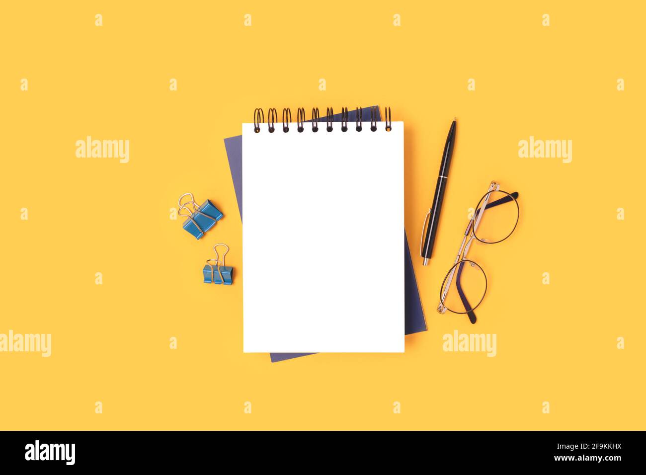 Spazio di lavoro con mockup per appunti, occhiali e cancelleria su sfondo giallo. Concetto scolastico con copyspace. Foto Stock