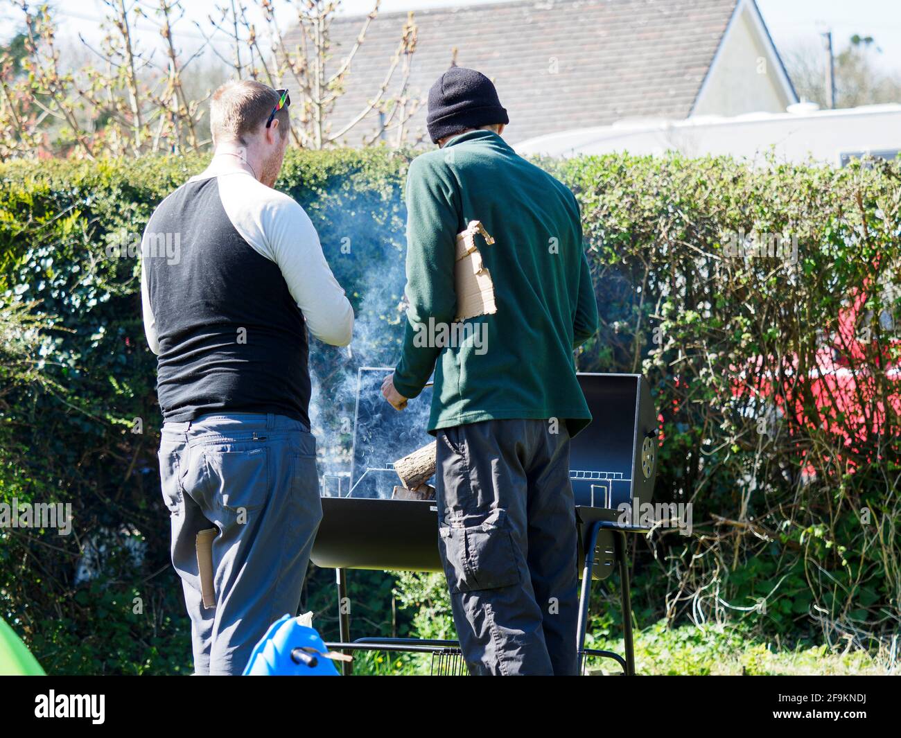 Due uomini che illuminano un barbecue nel giardino, Cornwall, Regno Unito Foto Stock