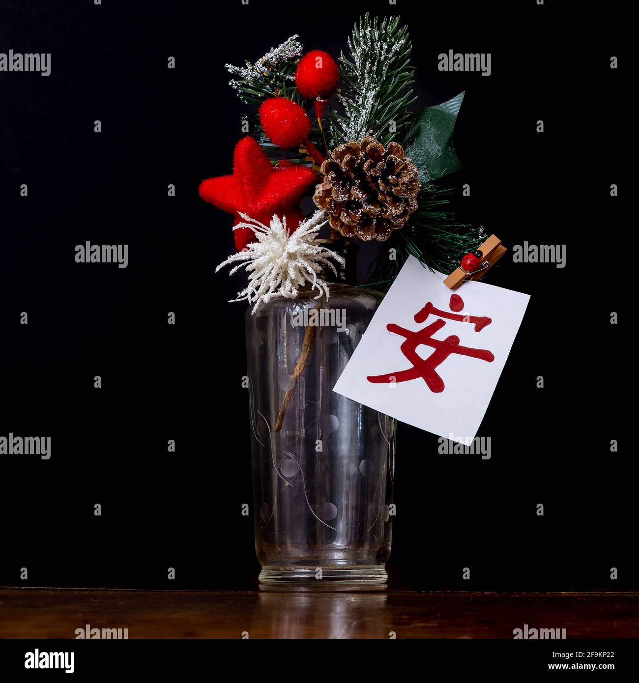 Un vaso di vetro con un cono di pino all'interno, alcuni rami di abete e decorazioni rosse, ha una carta con la scrittura cinese che significa serenità, come desiderio di t Foto Stock