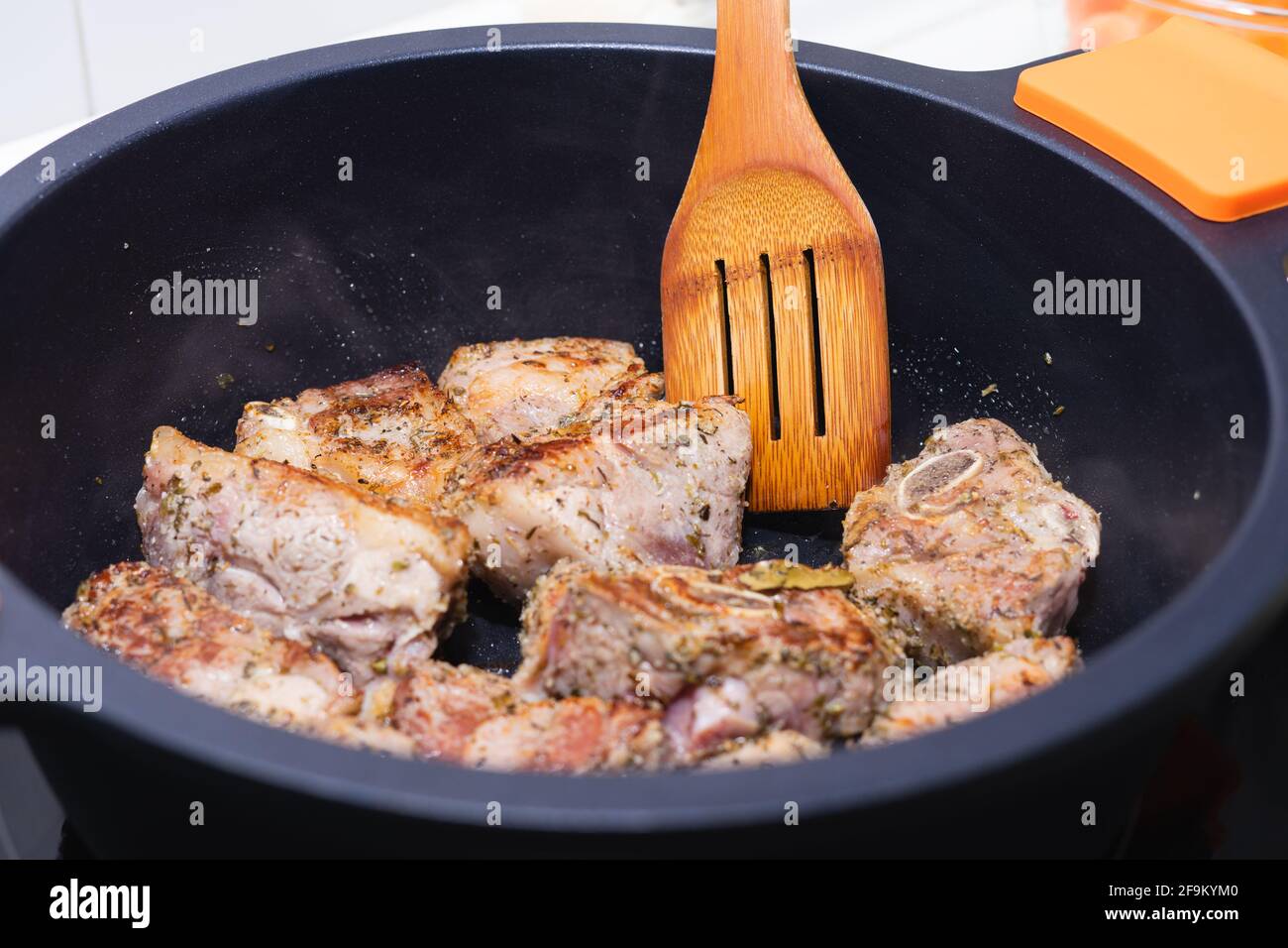 Carne cotta in un recipiente nero con utenil di legno. Concetto di cucina. Foto Stock