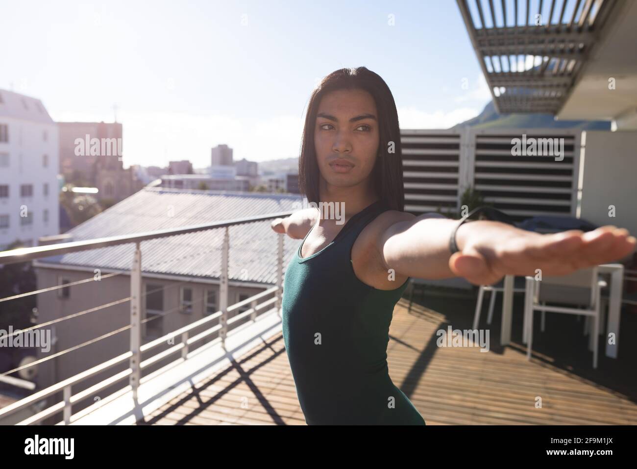 Razza mista transgender donna che pratica yoga in piedi sulla terrazza sul tetto al sole Foto Stock