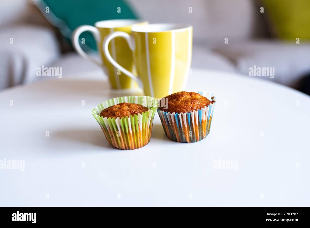 Muffin con involucri colorati e tazze verdi sulla parte superiore di un tavolo bianco Foto Stock