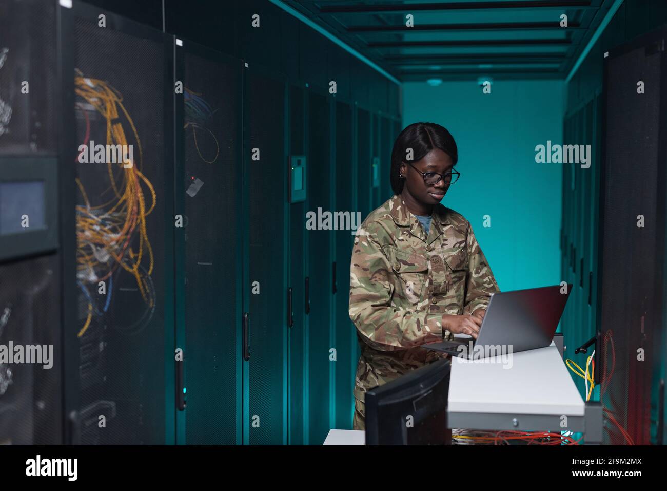 Ritratto di giovane afroamericana indossando uniforme militare utilizzando il computer durante la configurazione della rete in sala server, copia spazio Foto Stock