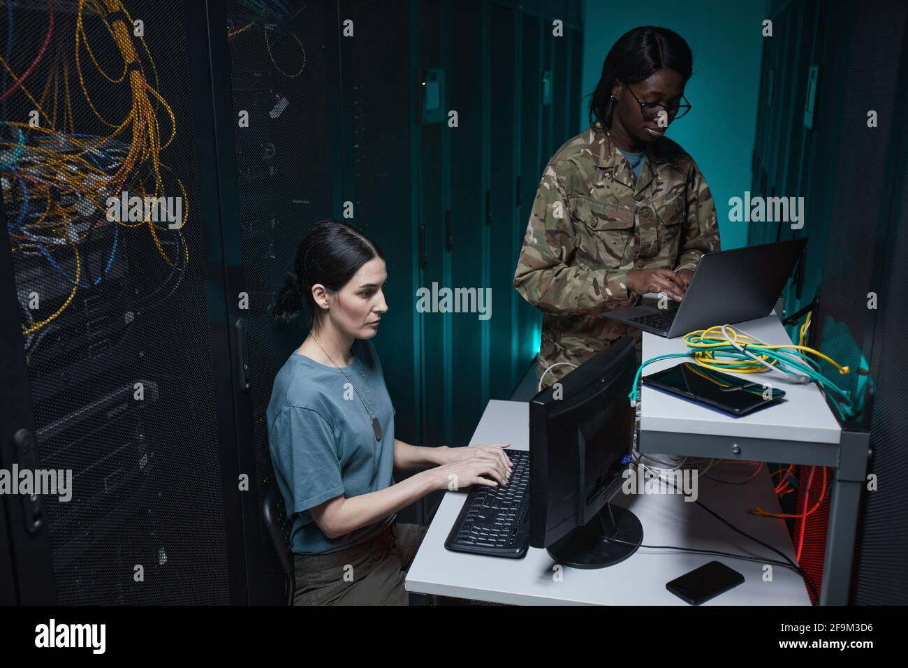 Ritratto di due giovani militari che usano computer mentre lavorano insieme nella stanza dei server e configurano la rete, copia spazio Foto Stock