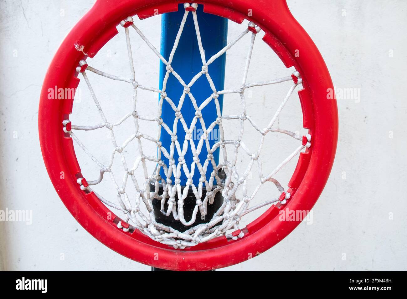 Un anello di cerchio rosso di plastica spesso con rete bianca attaccata a una tavola nera sul campo da basket di un bambino. Girato a Barbados, Caraibi. Piegato verso il basso. Foto Stock