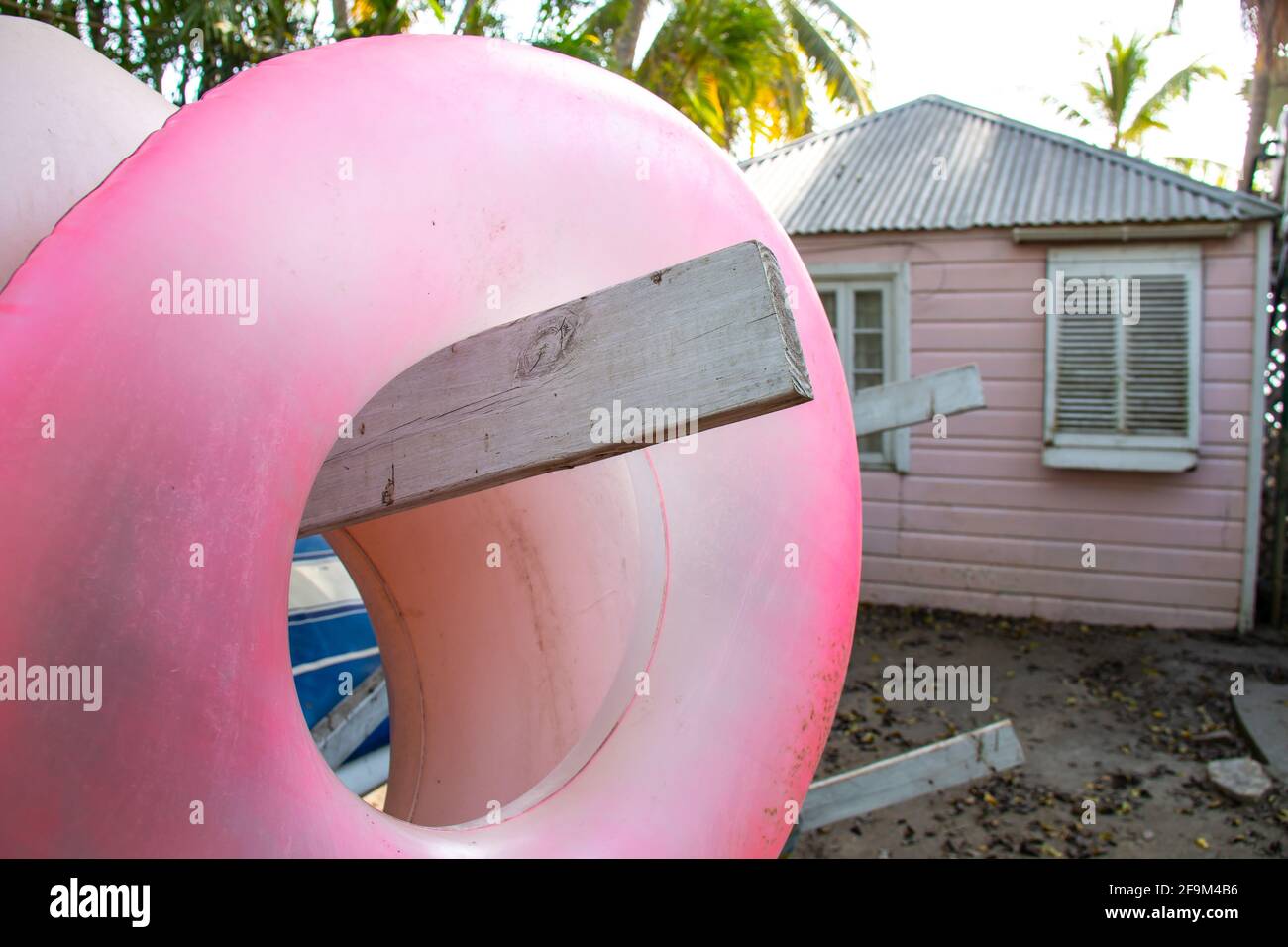 Ciambella ad anello gonfiabile rosa pastello appesa su una rastrelliera di legno contenente tavole da pagaia e kayak di fronte ad una casa di legno rosa. Foto Stock