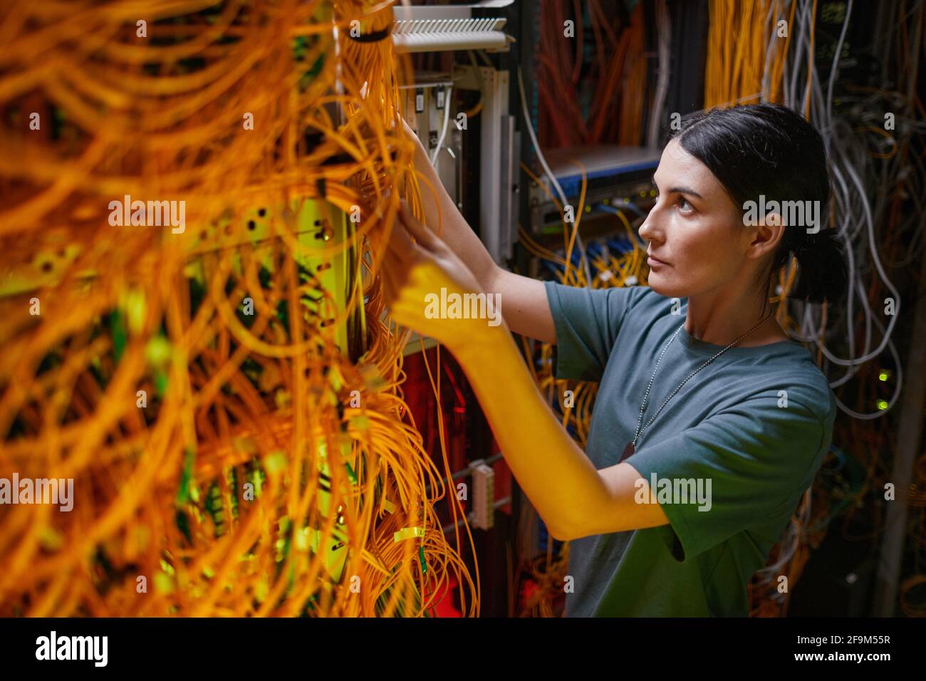 Vista laterale ritratto di giovane donna che indossa uniforme militare ispezionando il server durante il lavoro nella sala server, spazio di copia Foto Stock