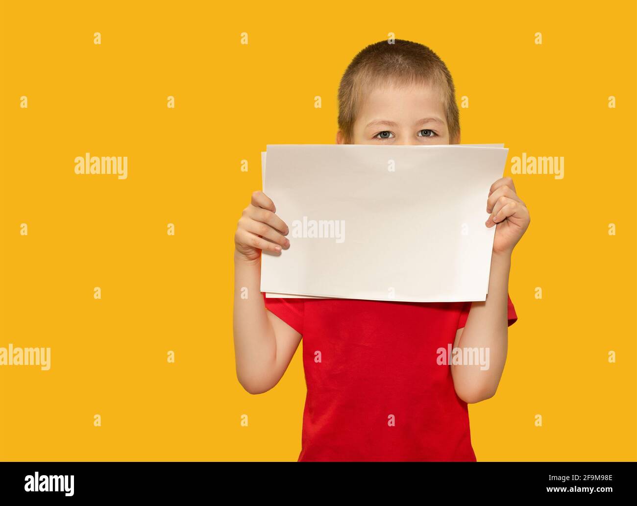 Un bambino, un ragazzo di 5 anni, in una T-shirt rossa, tiene fogli di carta su sfondo giallo. Concetto di spazio per il testo, lo spazio di copia, l'istruzione Foto Stock