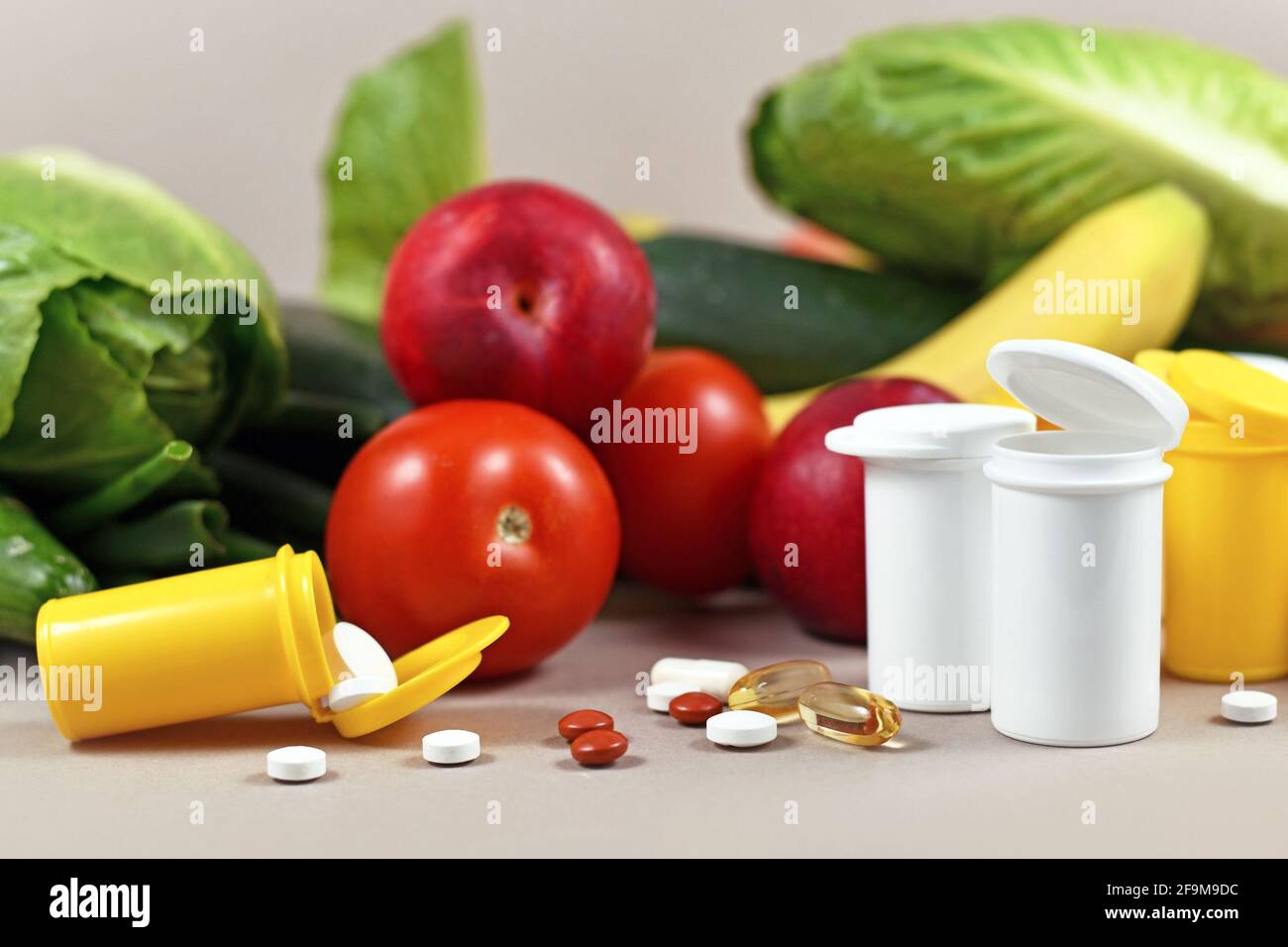 Bottiglie con pillole di integratori alimentari di fronte frutta e verdura sullo sfondo Foto Stock