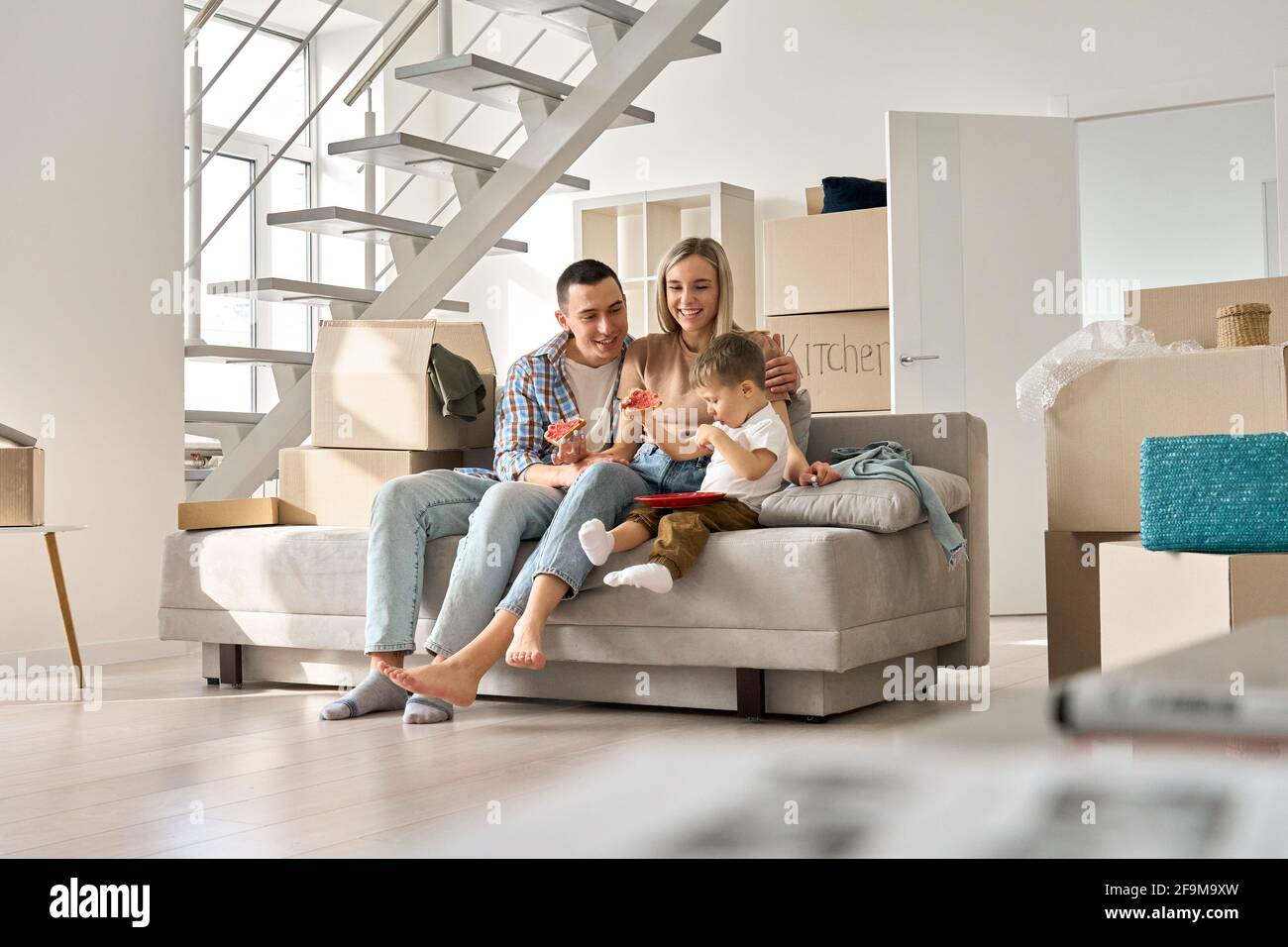 Felice famiglia coppia con bambino figlio rilassarsi sul divano in movimento giorno in nuova casa. Foto Stock