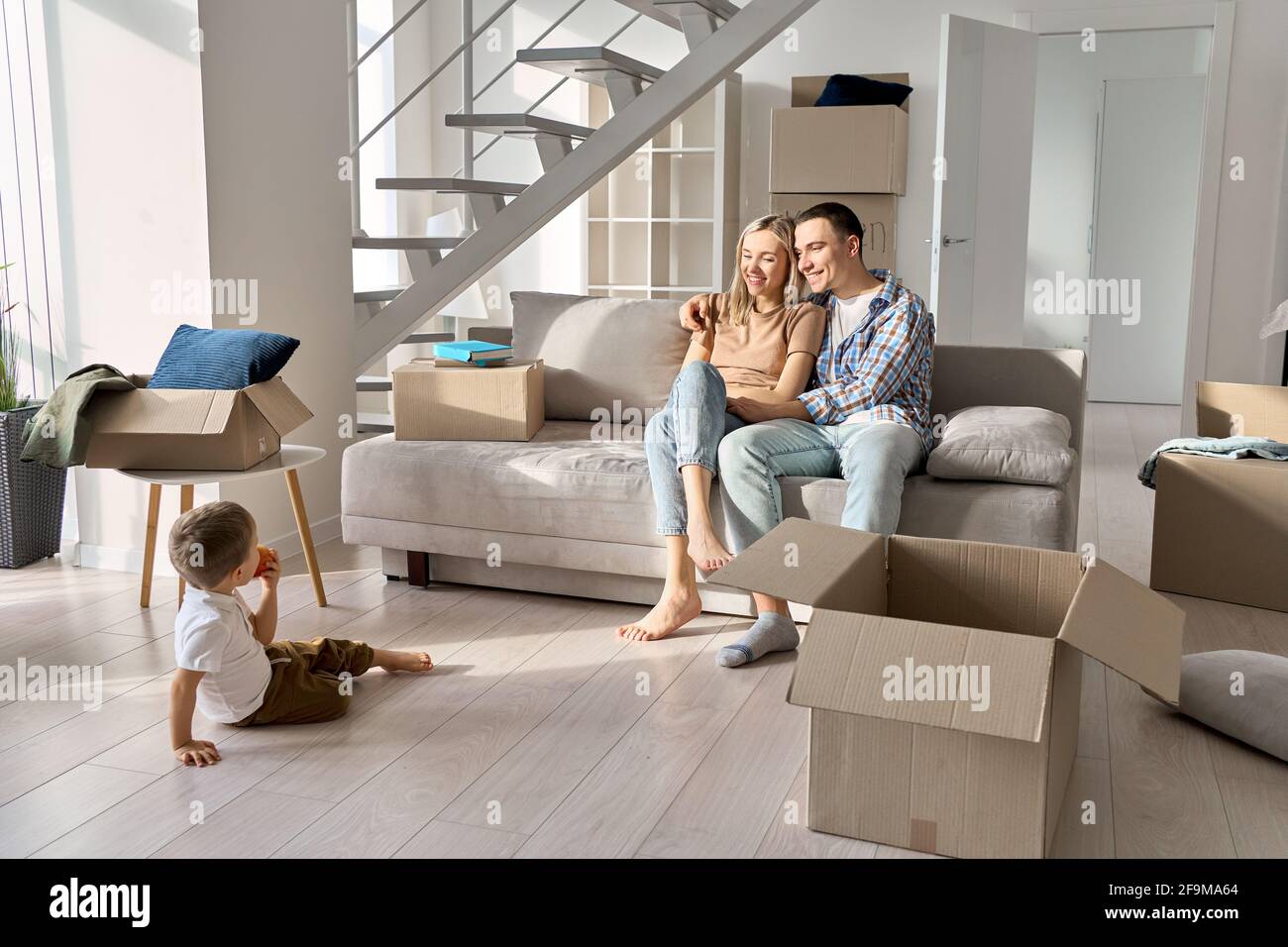 Famiglia felice nuovi proprietari di casa con bambino che si rilassa sul divano in giorno di movimento. Foto Stock
