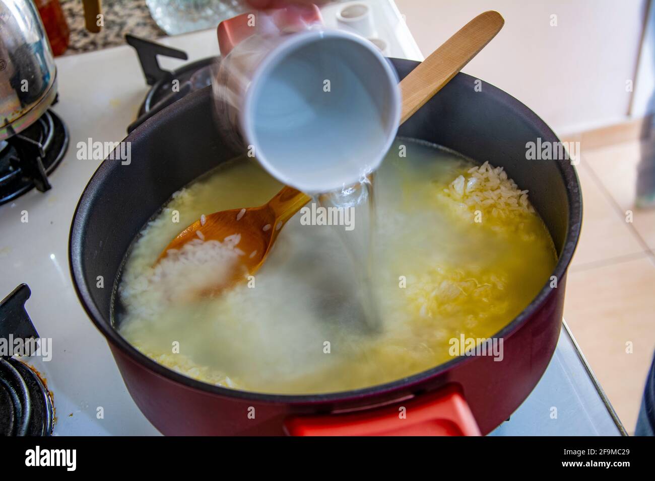 Aggiungendo acqua bollita al riso torrefatto in una pentola Foto Stock