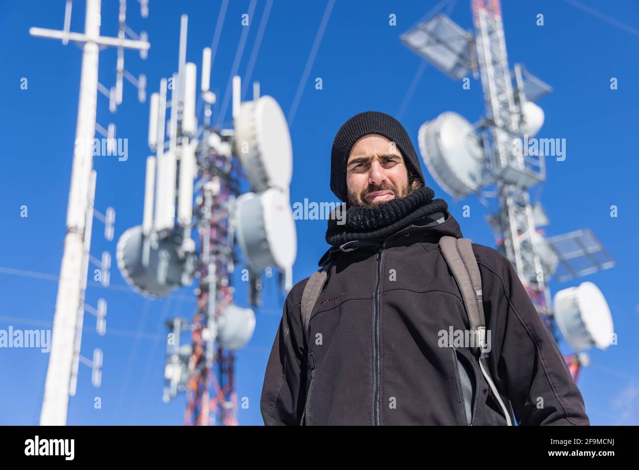 Un'immagine inclinabile di un giovane uomo che si trova di fronte a un'infrastruttura di telecomunicazione alta e complessa, con trasmettitori collegati. Foto Stock