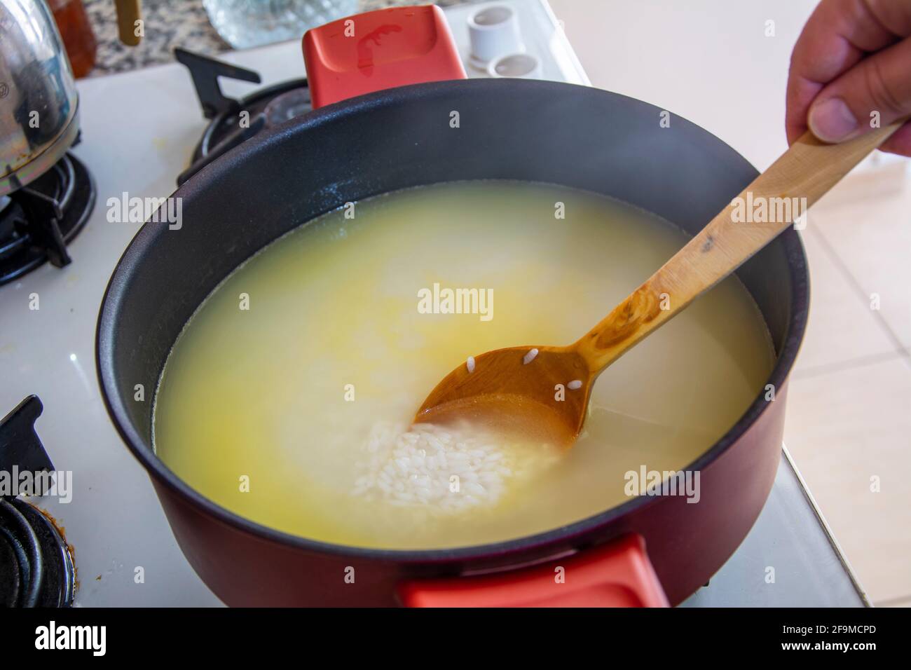 Mescolare la pentola con l'acqua versata sul riso con un cucchiaio di legno Foto Stock