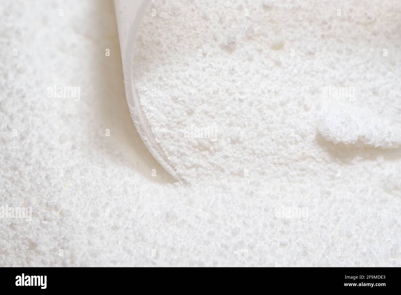 Polvere detergente bianca pura per bucato, aggrappata e raccolta da un misurino in plastica trasparente. Immagine luminosa e super macro prospettiva Foto Stock