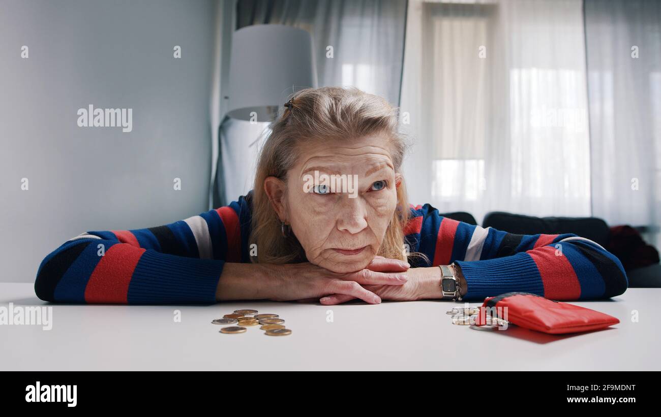 Anziana pensionato disperata che guarda una piccola quantità di monete sul tavolo. Foto di alta qualità Foto Stock