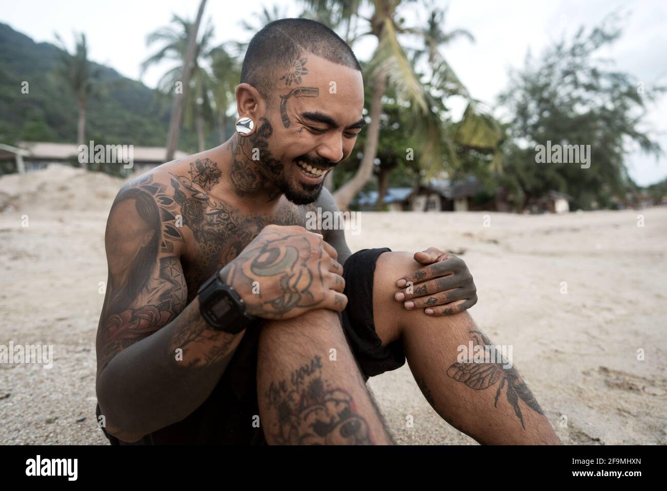 ragazzo hipster con tatuaggio seduto sulla spiaggia in thailandia Foto Stock
