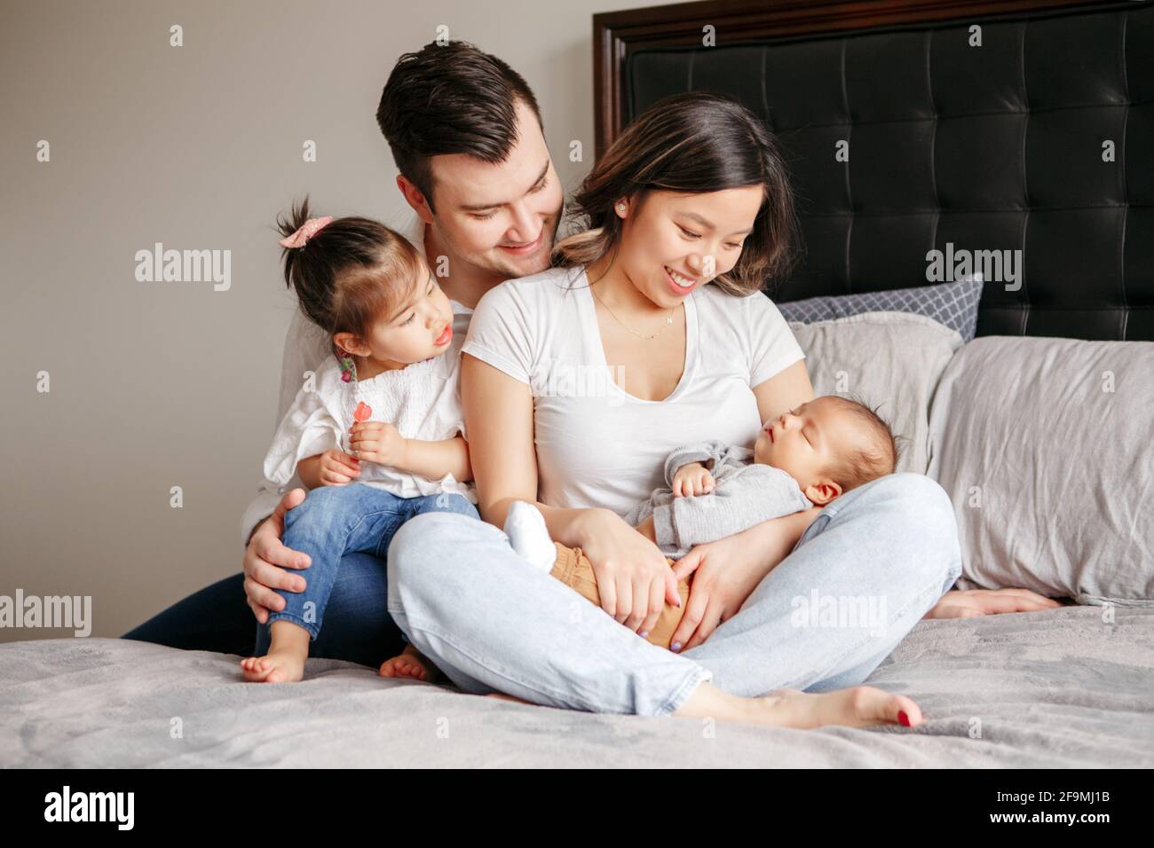 Famiglia multirazziale con due bambini piccoli a letto a. casa Foto Stock