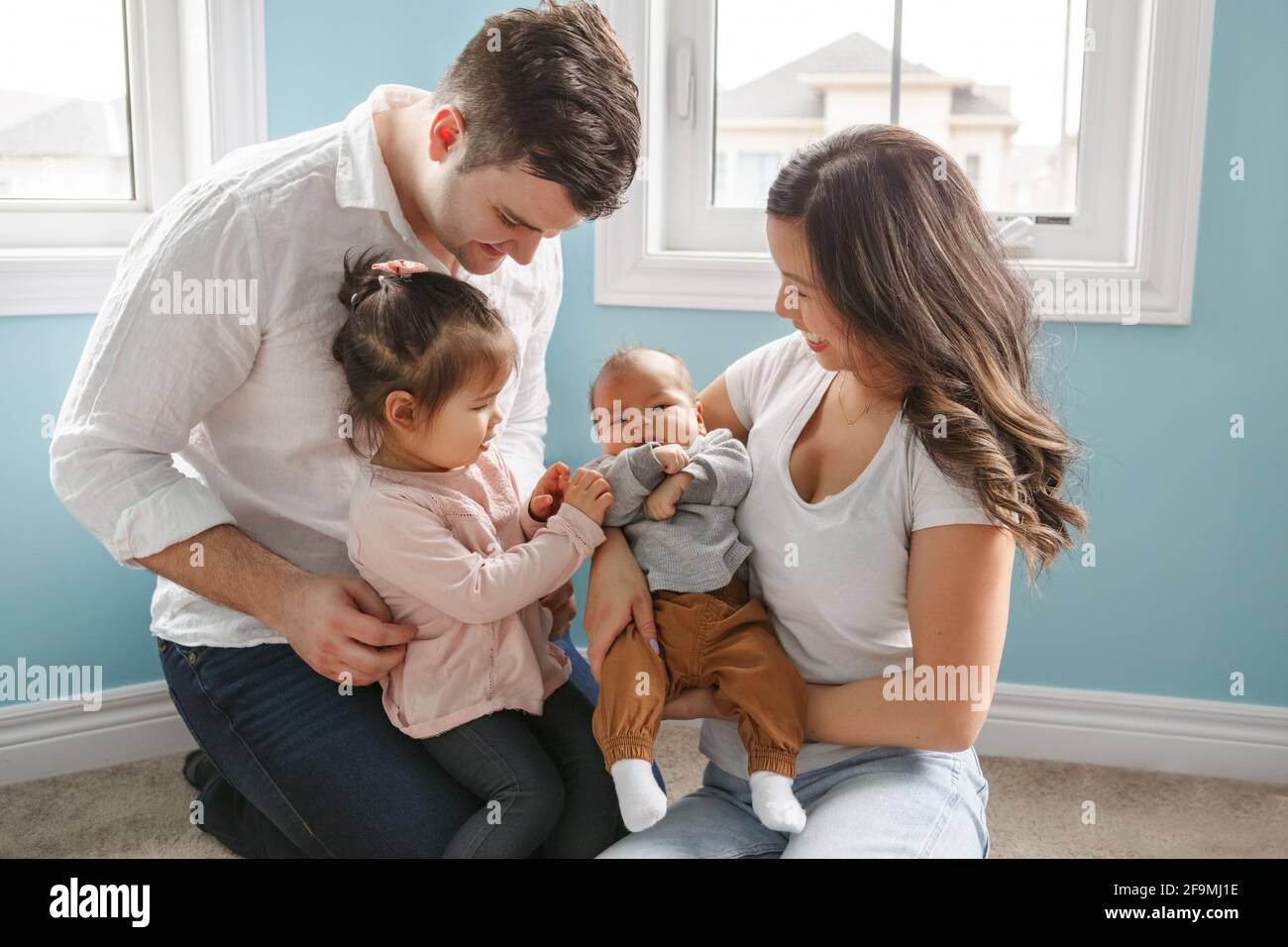 Famiglia felice con i bambini a casa. La sorella maggiore incontra il fratello neonato Foto Stock