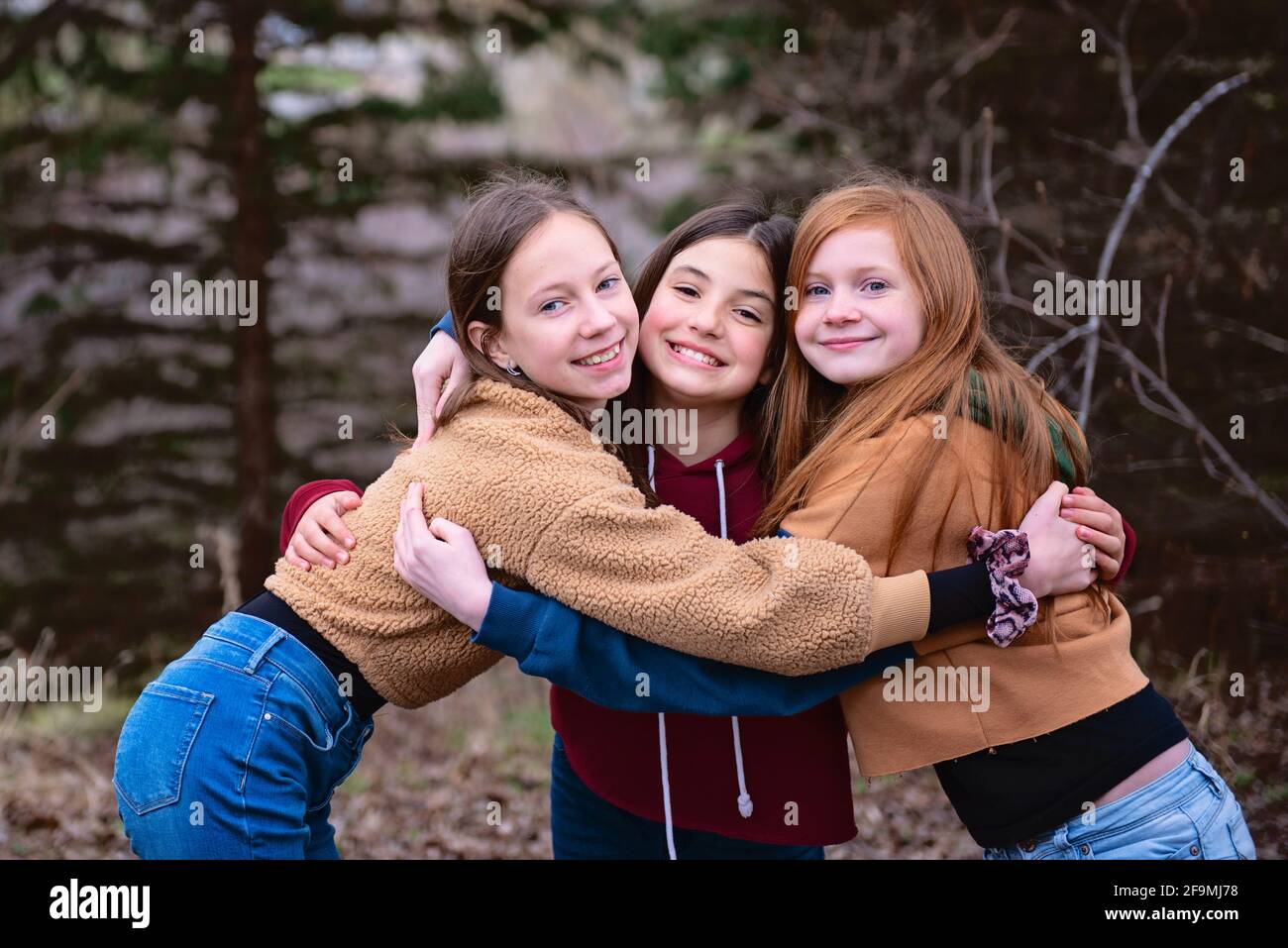 Tre ragazze di Tween che si levano in piedi all'aperto abbracciandosi l'un l'altro. Foto Stock