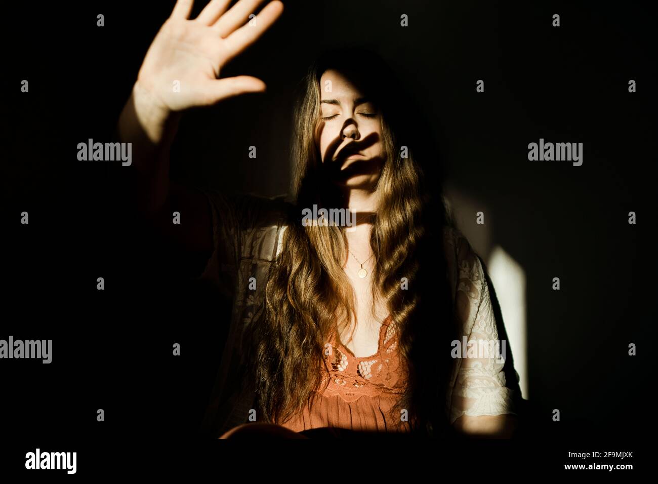Una donna che tiene la sua mano alla luce che casting a. ombra sul viso Foto Stock