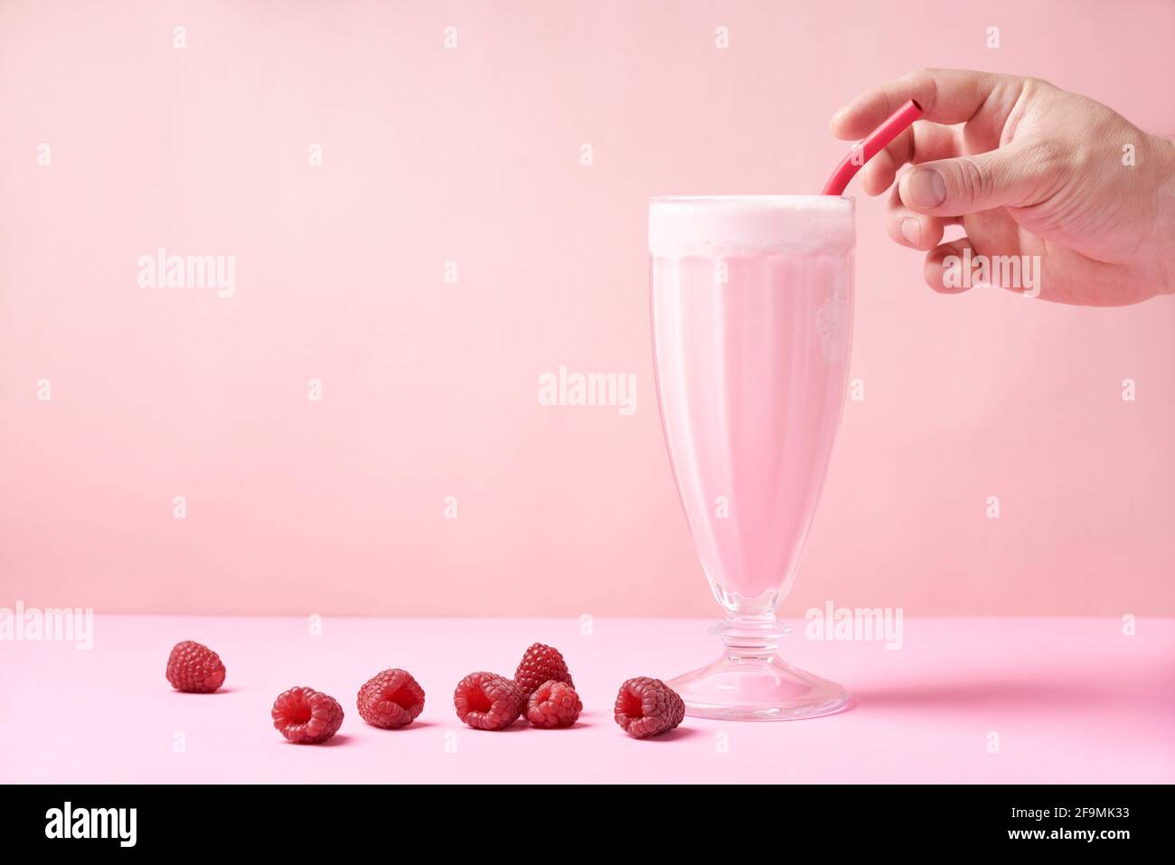 Una mano afferra una cannuccia metallica riutilizzabile eco-friendly che è in una frullato di lampone Foto Stock