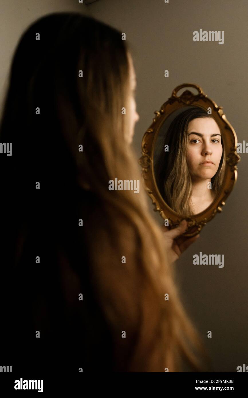 Una donna che si guarda in uno specchio d'epoca Foto Stock