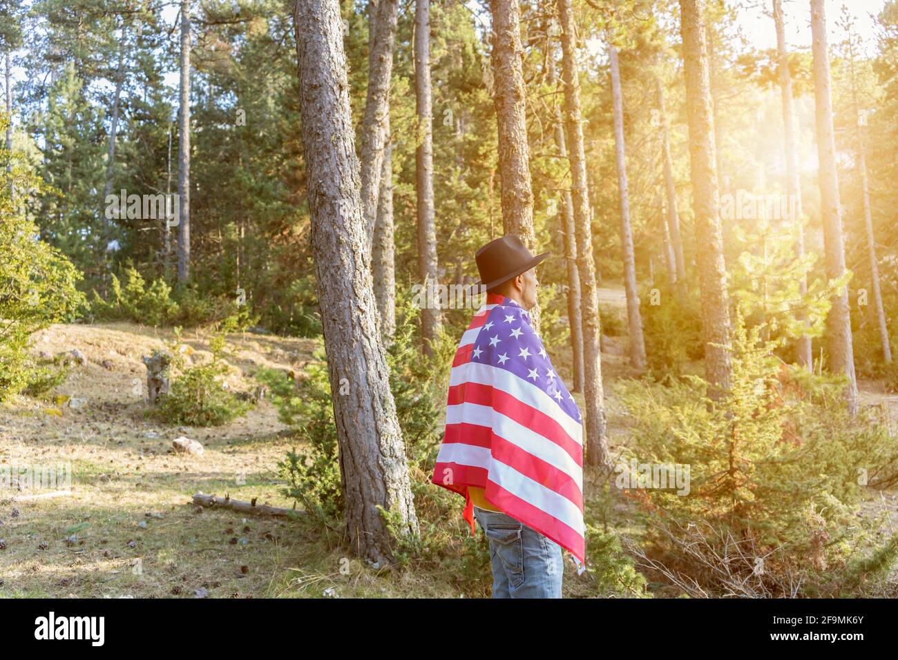 Concetto di festa del giorno dell'indipendenza degli Stati Uniti, 4 luglio.Man in cappello nero cowboy che tiene bandiera americana al tramonto nel parco della foresta. Foto Stock