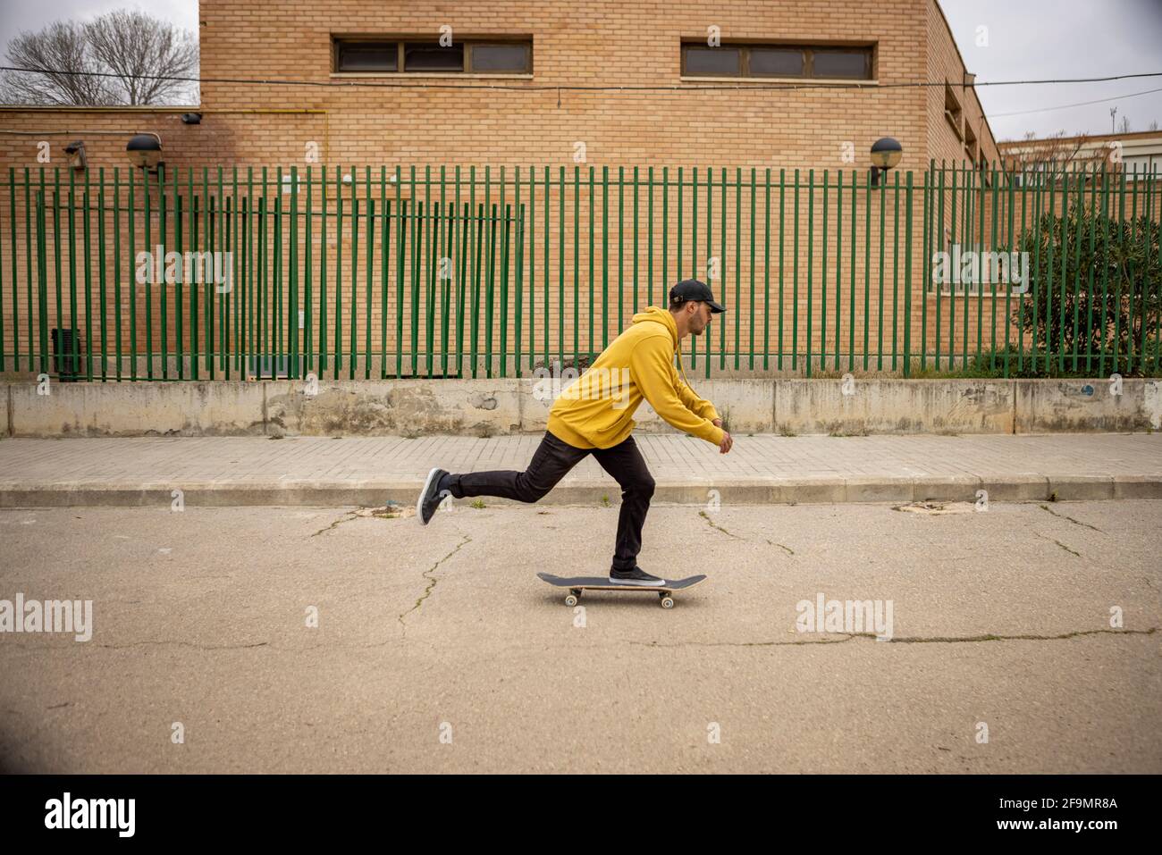 Un giovane uomo skateboard sulla strada in un giallo felpa con cappuccio e cappuccio nero Foto Stock