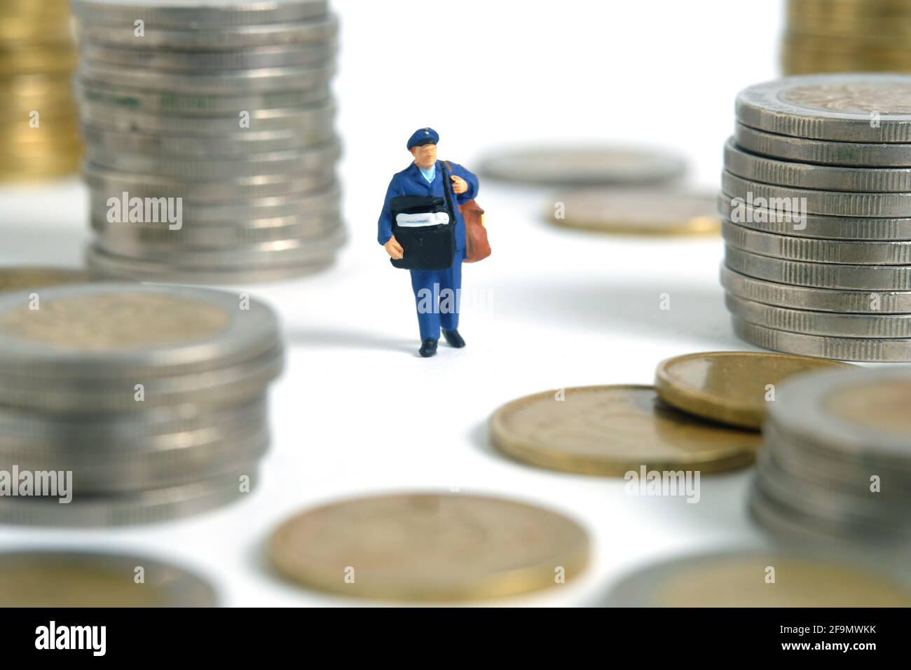 Fotografia concettuale dei giocattoli delle persone in miniatura. Pagamento in contanti al momento della consegna e spese di spedizione. Corriere postino in piedi tra pila di moneta, isolato Foto Stock