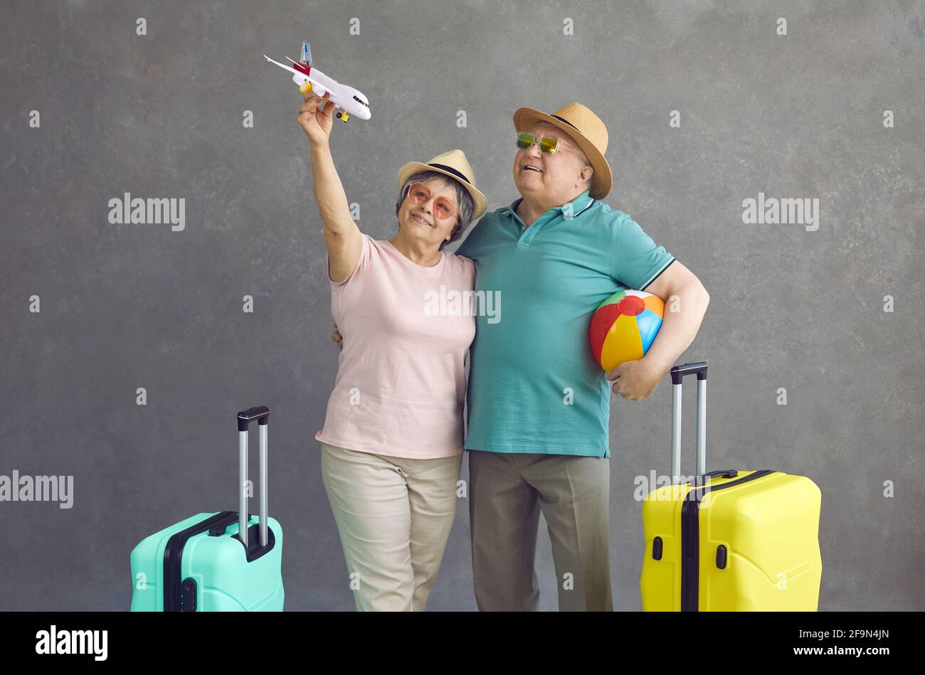 Studio di felice coppia senior in occhiali da sole e cappelli tenendo un aeroplano di carta Foto Stock