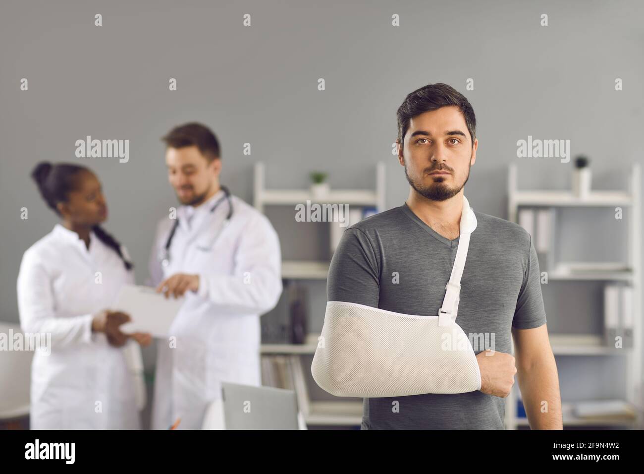 Paziente uomo serio con braccio rotto avvolto su bendaggio ortopedico verticale Foto Stock