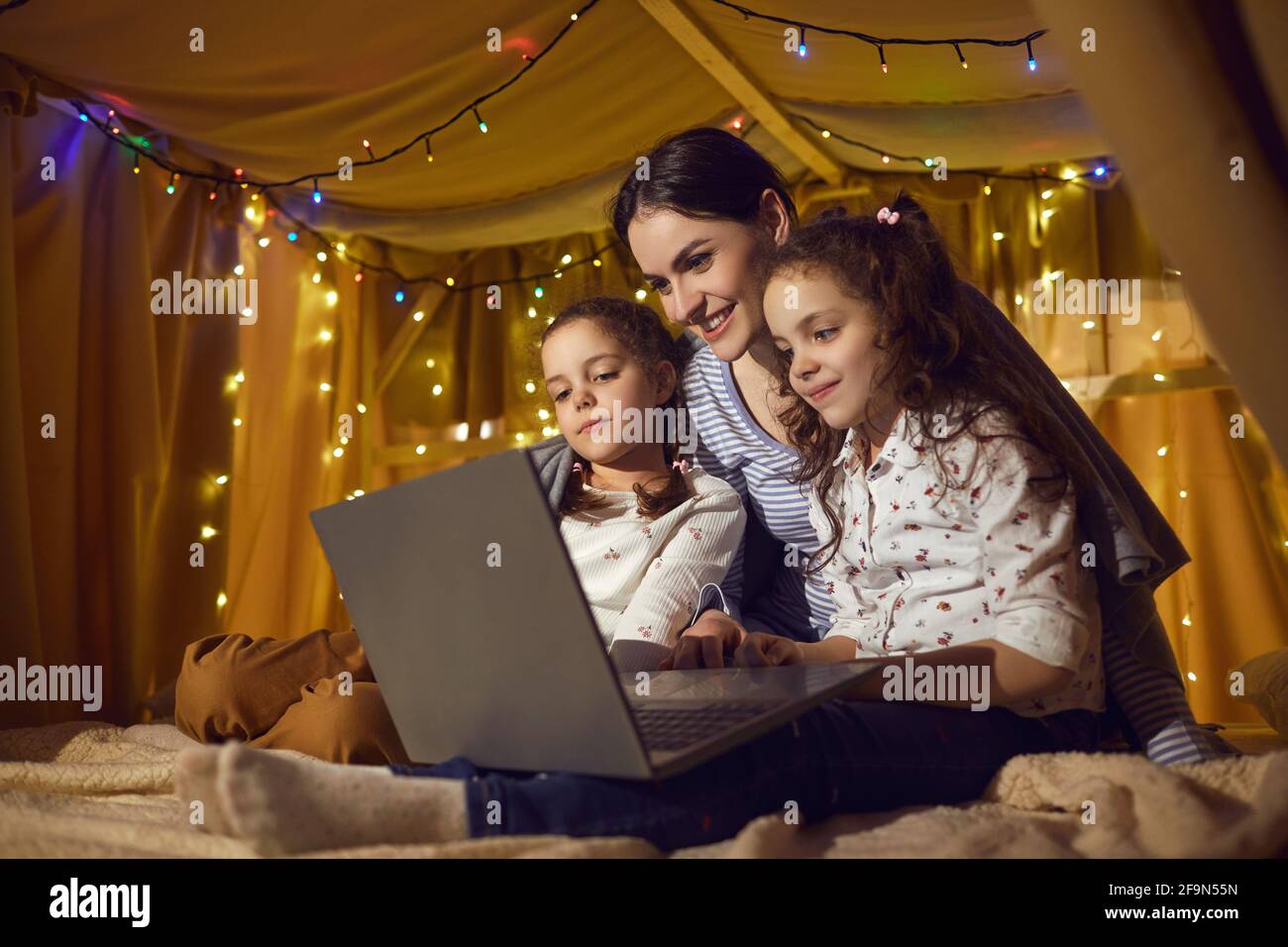 Madre e due figli figlie che guardano divertenti cartoni animati su un computer portatile prima di coricarsi Foto Stock