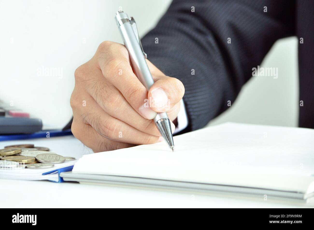 Mano di uomo d'affari che tiene una scrittura della penna sul libro - concetto commerciale e finanziario Foto Stock