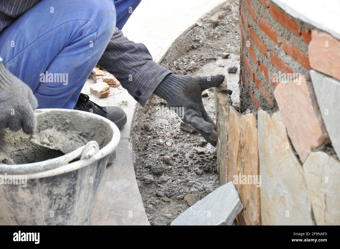 Lavoratore di costruzione che installa le piastre di pietra sulla parete di mattone con mortaio Foto Stock