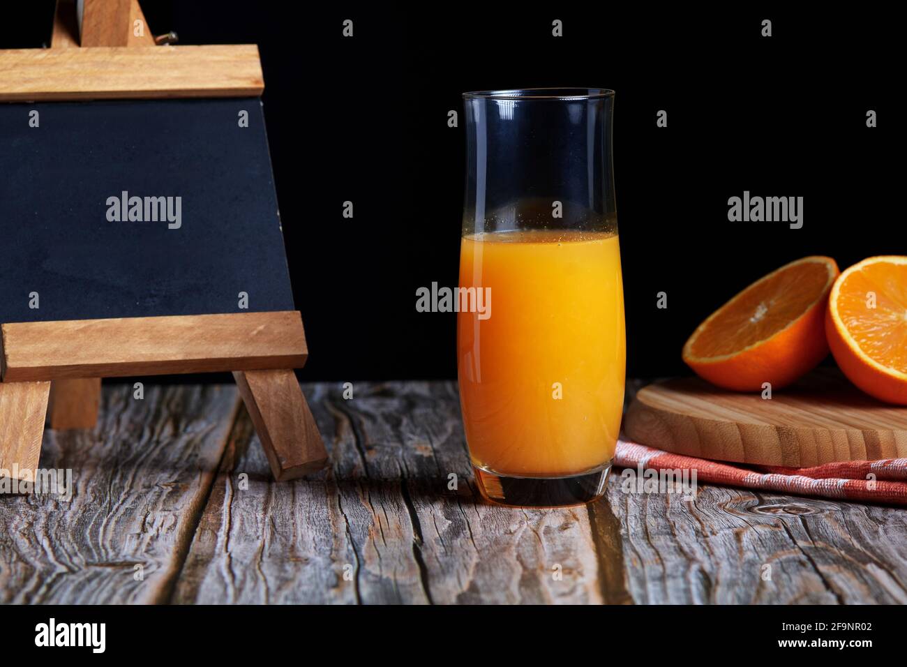Caraffa di succo d'arancia fresco appena spremuto con frutta fresca su tavolo di legno. Piccola lavagna per spazio copia e sfondo nero Foto Stock
