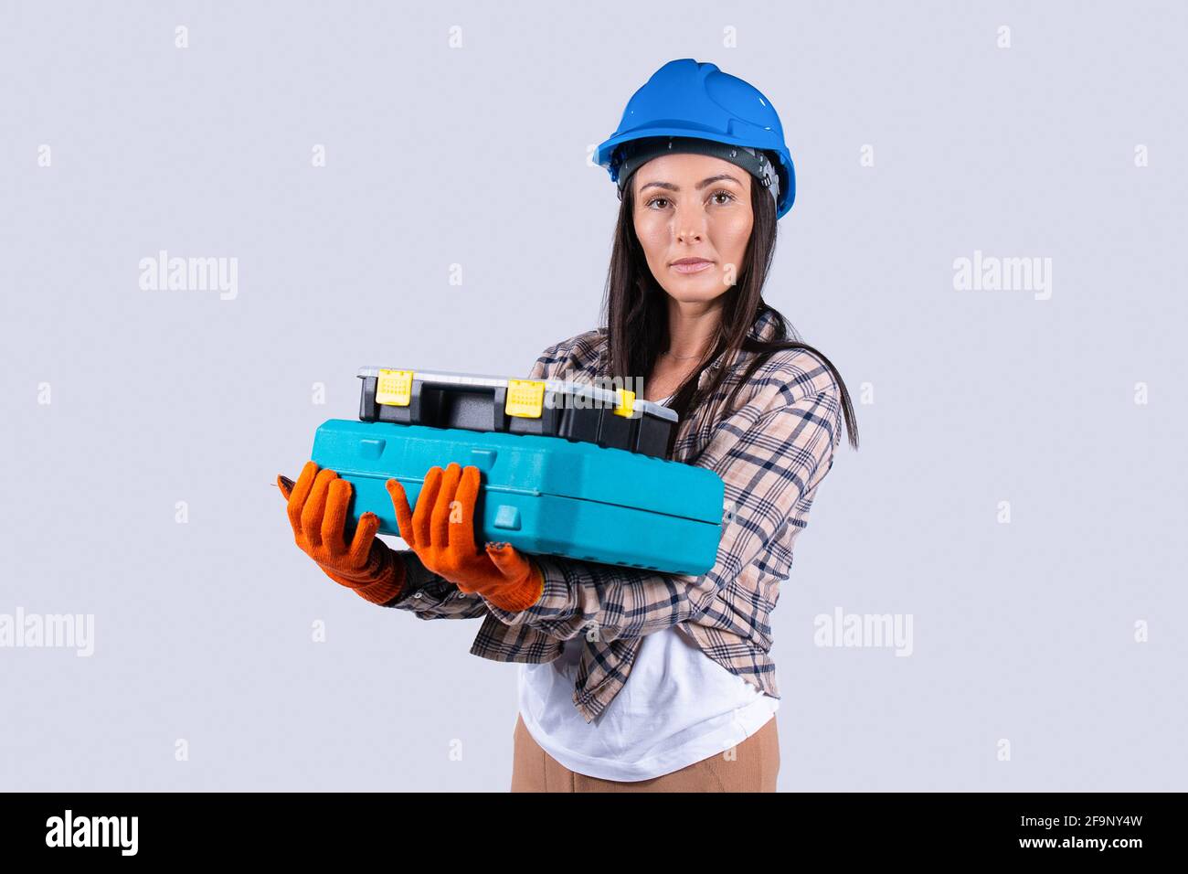Donna caucasica che guarda serio al toolkit di tenuta della telecamera in officina isolato sfondo grigio. Ingegneria femminile e concetto industriale Foto Stock