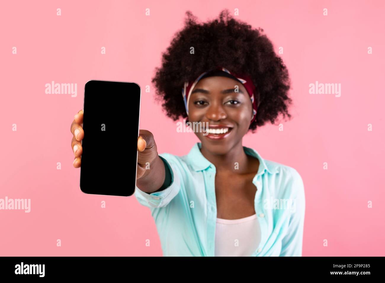 Black Bushy Lady che mostra lo schermo del telefono su sfondo rosa Foto Stock
