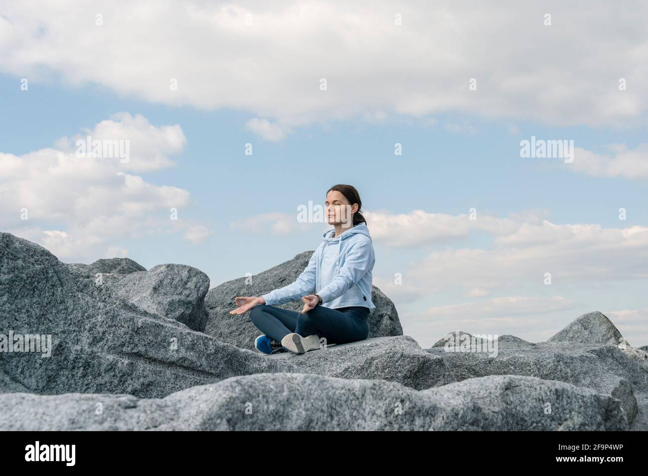 Donna che medita, pratica yoga e pranayama. Posa del loto. Gyan mudra. Seduta su cima rocciosa. Foto Stock