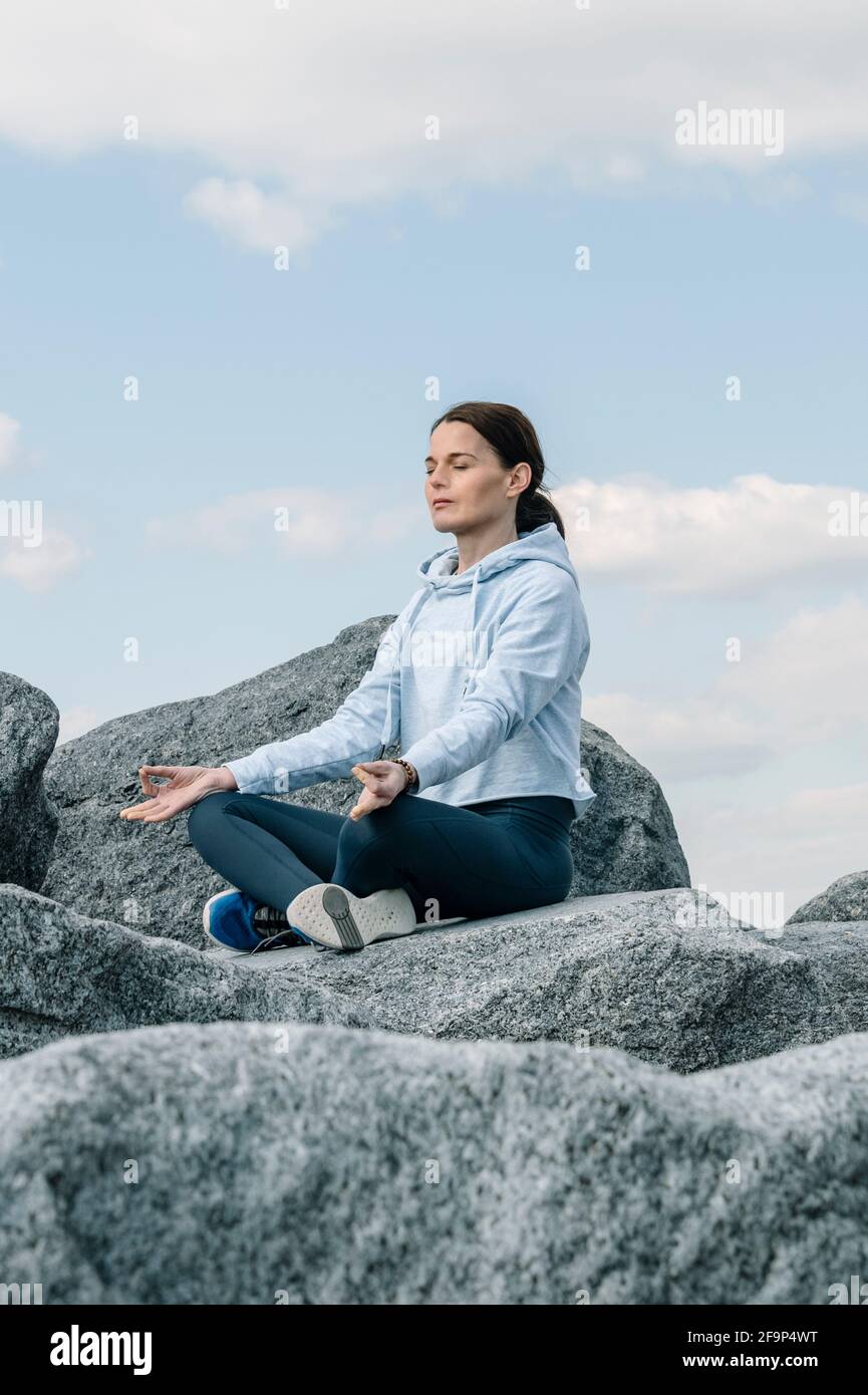 Donna che medita, pratica yoga e pranayama. Posa del loto. Gyan mudra. Seduta su cima rocciosa. Foto Stock