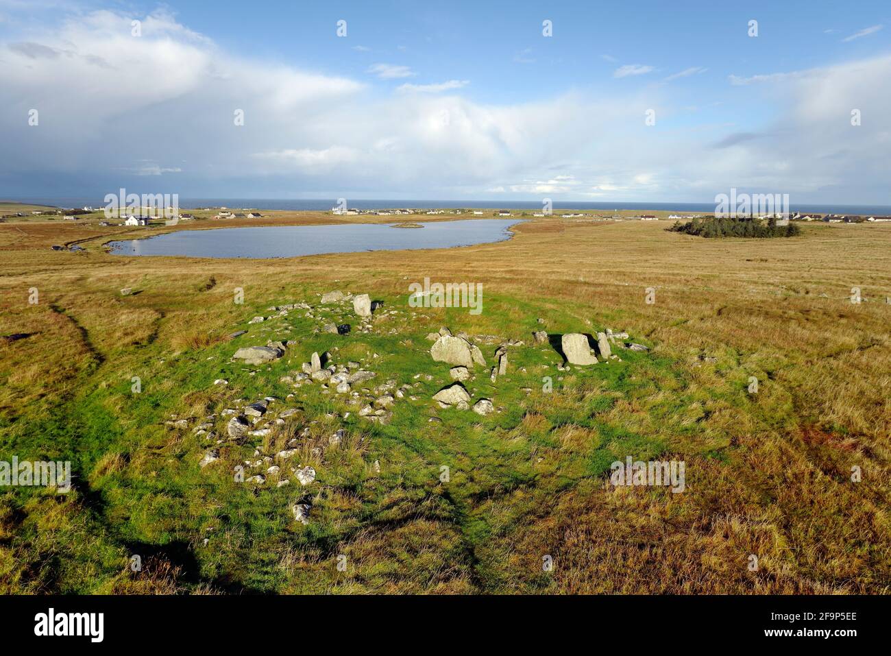 Sito preistorico Steinacleit, Isola di Lewis. Resti di cairn centrale chambered. Anello in pietra a basso cerchio visibile a metà distanza con crannog dietro Foto Stock